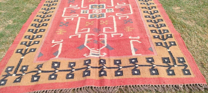 May include: A red, brown, and black patterned rug with a geometric design. The rug has a fringe border.