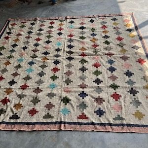 May include: A large, rectangular rug with a cream-coloured background and a repeating pattern of colourful diamond shapes. The rug has a dark blue border.