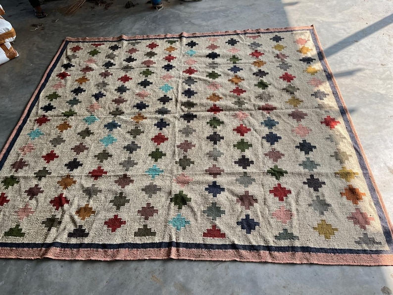 May include: A large, rectangular rug with a cream-coloured background and a repeating pattern of colourful diamond shapes. The rug has a dark blue border.