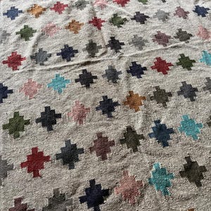 May include: A beige rug with a geometric pattern of colourful crosses. The crosses are in shades of red, blue, green, and brown.