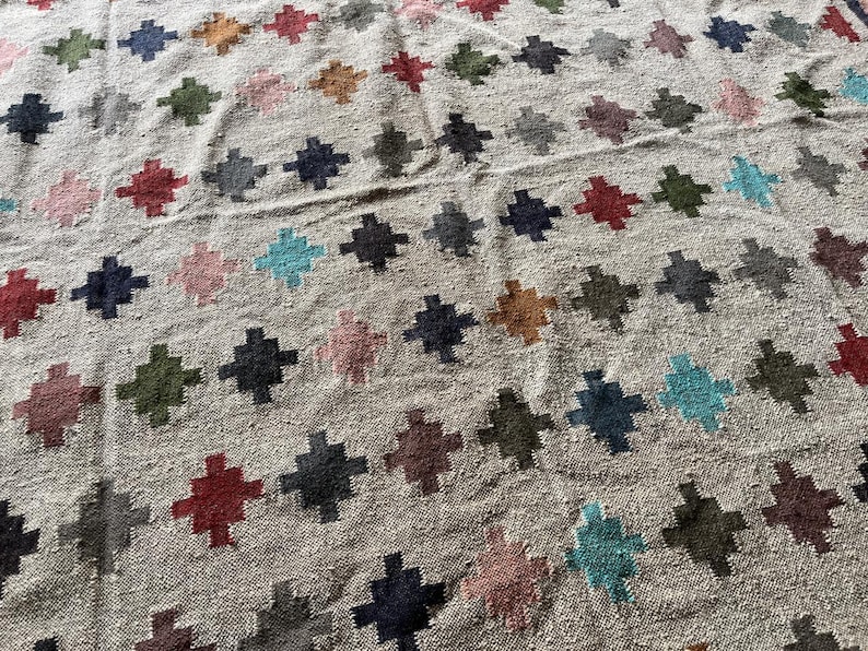 May include: A beige rug with a geometric pattern of colourful crosses. The crosses are in shades of red, blue, green, and brown.