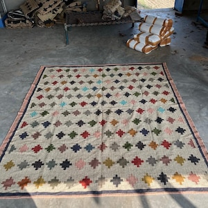 May include: A large, rectangular rug with a geometric pattern of colourful squares and diamonds. The rug is made of natural fibres and has a rustic, hand-woven look.