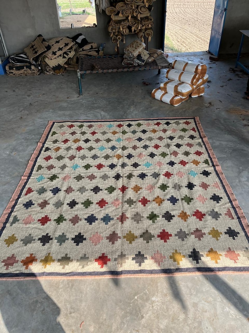 May include: A large, rectangular rug with a geometric pattern of colourful squares and diamonds. The rug is made of natural fibres and has a rustic, hand-woven look.