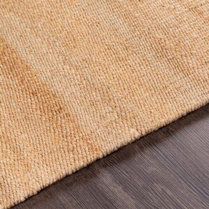 Op de afbeelding: Een close-up van een vloerkleed van natuurlijke vezels met een geweven textuur. Het vloerkleed is licht beige van kleur.