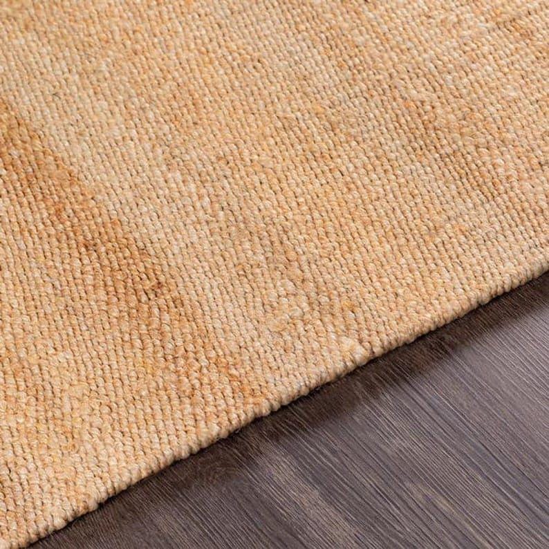 Op de afbeelding: Een close-up van een vloerkleed van natuurlijke vezels met een geweven textuur. Het vloerkleed is licht beige van kleur.