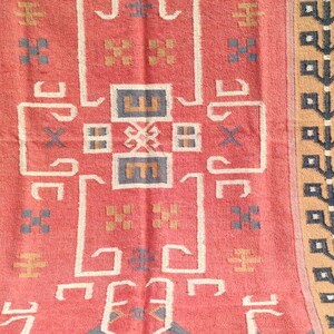 May include: A red, brown, and black patterned rug with a geometric design. The rug has a fringe border.