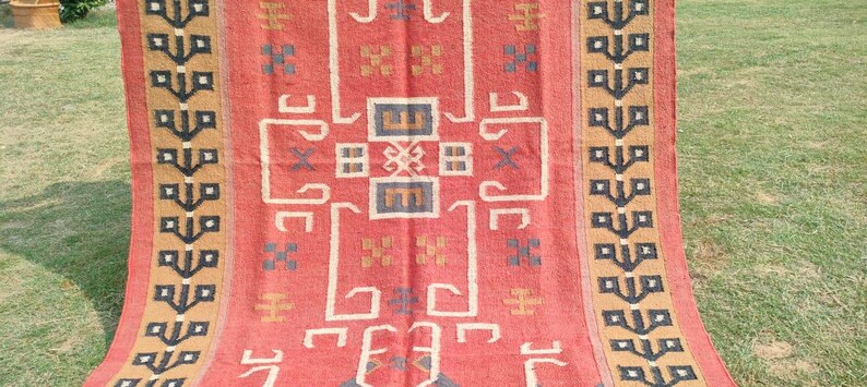 May include: A red, brown, and black patterned rug with a geometric design. The rug has a fringe border.