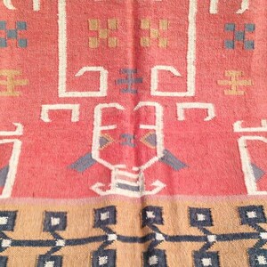 May include: A vintage rug with a geometric pattern in shades of red, brown, and black. The rug has a central design with a repeating pattern of stylized trees and geometric shapes.
