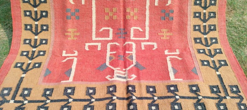 May include: A vintage rug with a geometric pattern in shades of red, brown, and black. The rug has a central design with a repeating pattern of stylized trees and geometric shapes.