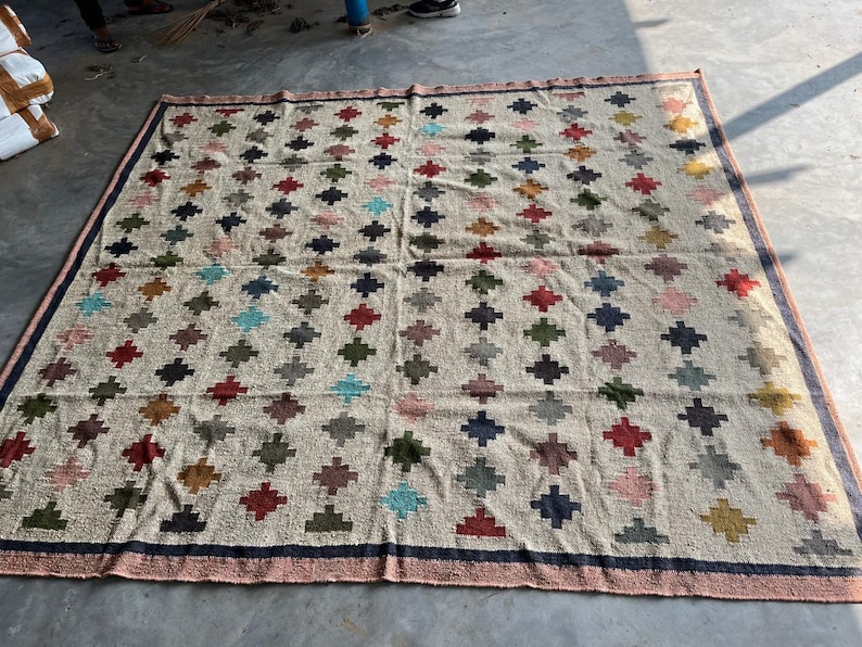 May include: A large, rectangular rug with a cream-coloured background and a geometric pattern of colourful diamonds. The diamonds are arranged in a grid pattern and are made of different colours, including red, blue, green, and yellow.