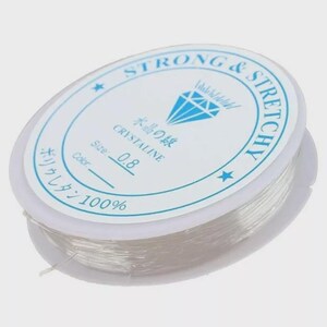 May include: A spool of clear, elastic beading cord. The white label reads "STRONG & STRETCHY" and "CRYSTALINE" with Japanese text. The cord size is 0.8. The label also indicates the cord is 100% polyurethane.