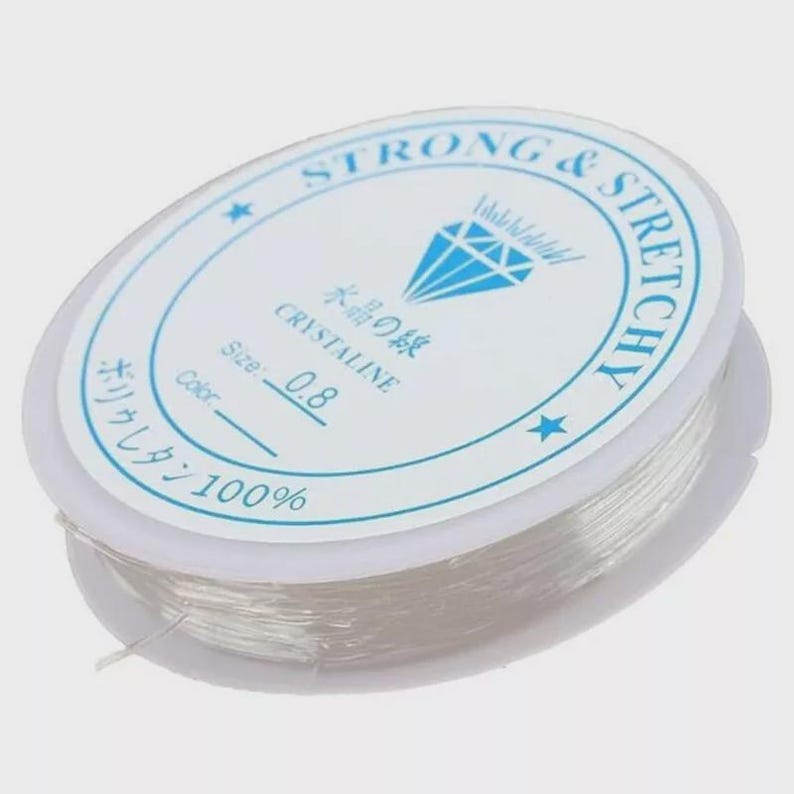 May include: A spool of clear, elastic beading cord. The white label reads "STRONG & STRETCHY" and "CRYSTALINE" with Japanese text. The cord size is 0.8. The label also indicates the cord is 100% polyurethane.