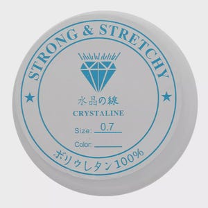 May include: A white spool of strong and stretchy crystalline thread. The label features blue text and a diamond graphic. Text includes "STRONG & STRETCHY", "水晶の線", "CRYSTALINE", "Size: 0.7", and "ボリウレタン100%"