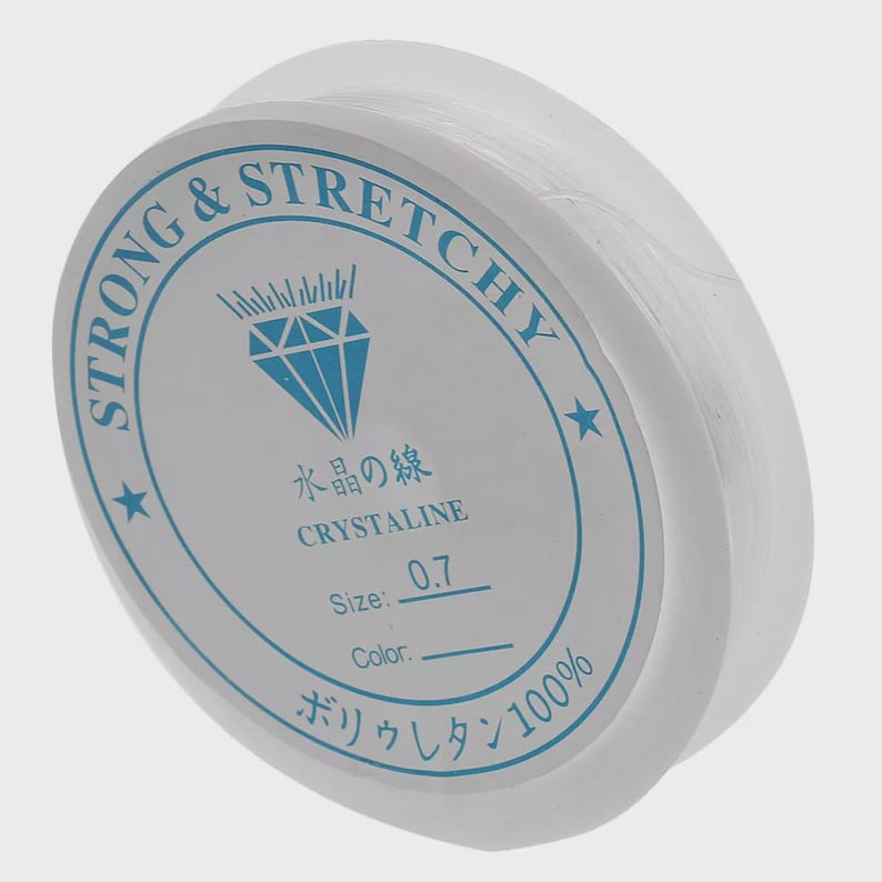 May include: A spool of clear, stretchy beading cord. The white label features blue text and a diamond graphic, with the words "STRONG & STRETCHY" and "CRYSTALINE". The size is 0.7.