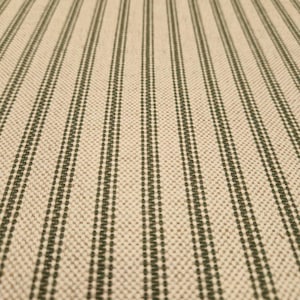 May include: Close-up of a beige fabric with thin green stripes. The fabric has a woven texture and a subtle sheen.
