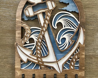 Könnte beinhalten: Schlüsselhalter aus Holz mit einem Design aus weißem Anker und blauen Wellen. Der Anker ist von einem Seilmuster umgeben. Am unteren Ende des Schlüsselhalters befinden sich fünf Haken.