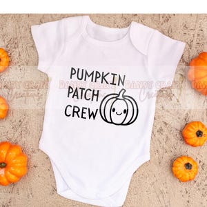 May include: White baby bodysuit featuring the words "PUMPKIN PATCH CREW" and a smiling pumpkin illustration in black. Small orange pumpkins are scattered around the bodysuit, ideal for autumn.