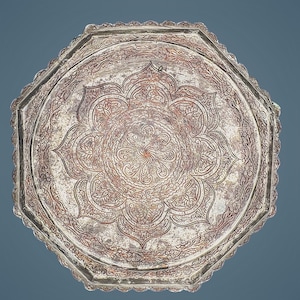 May include: An octagonal silver-toned metal tray featuring an intricate engraved floral pattern. The centre displays a large stylised lotus motif surrounded by concentric circles of detailed scrollwork and a scalloped, decorative border edge.