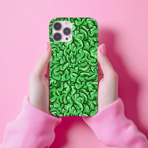 May include: A green phone case with a repeating abstract pattern of swirling shapes. The case is held against a pink background. The phone case has a camera cutout.