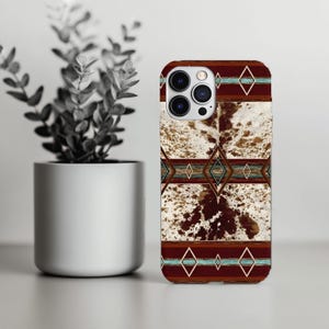 May include: A phone case with a brown, white, and turquoise geometric design. The case has a cowhide pattern in the center, with brown and turquoise diamond shapes. The top and bottom of the case are a dark brown color.