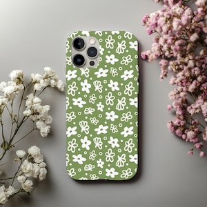 May include: A green phone case with a white floral pattern. The case features a repeating design of various flower shapes and dots. The phone case is shown on a gray surface with white and pink flowers in the background.
