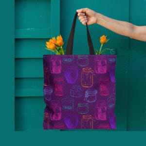 May include: A purple tote bag with a repeating pattern of sketched jars in various colors. The bag has black handles and is held by a person. Orange flowers are visible inside the bag.