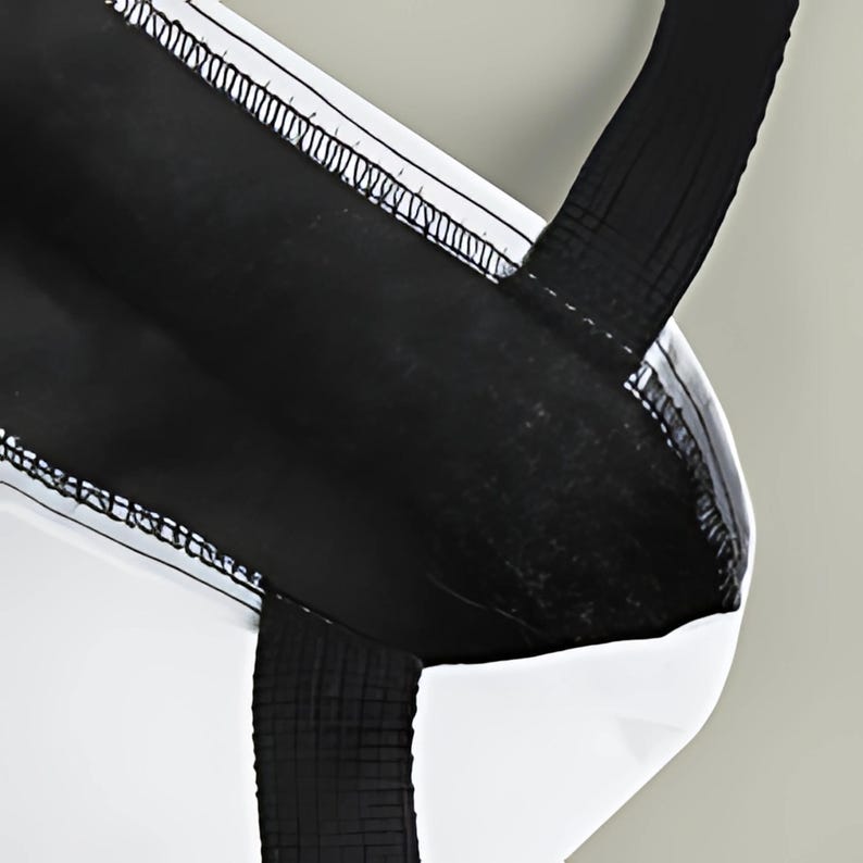 May include: A black and white tote bag with a rectangular shape. The bag features a black body with white accents and a black handle. The stitching is visible along the edges.