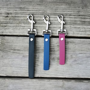 May include: Three leather keychains with silver swivel clips. The keychains are black, blue, and pink.