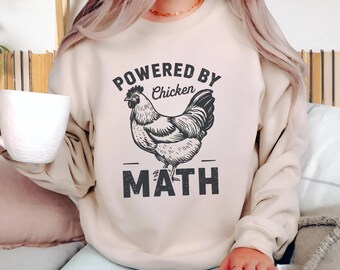 Może przedstawiać: Beżowa bluza z okrągłym dekoltem z czarną grafiką kurczaka pośrodku. Nad kurczakiem znajduje się napis "POWERED BY Chicken", a pod nim słowo "MATH" wydrukowane dużymi, pogrubionymi, postarzanymi czarnymi literami.