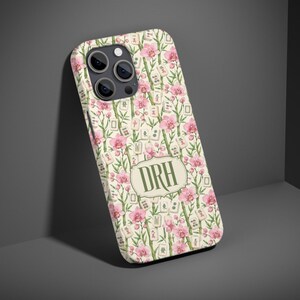 May include: A smartphone case featuring a pattern of pink orchid flowers, green bamboo stalks, and mahjong tiles. In the centre, a decorative light-coloured label displays the letters DRH in a dark green serif font. The case has a camera cutout.