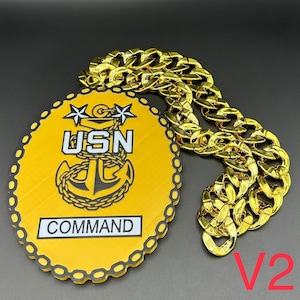 May include: A gold chain necklace with a large, yellow oval pendant. The pendant has a black anchor with the text "USN COMMAND" in white.