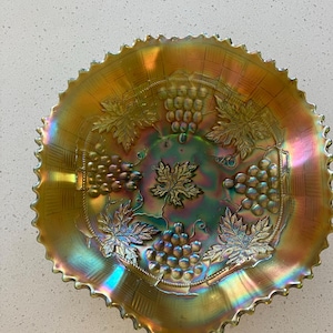 May include: A vintage iridescent glass bowl with a grapevine design. The bowl has a scalloped edge and is decorated with clusters of grapes and leaves.