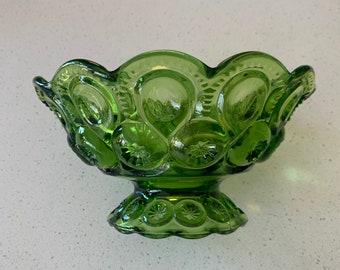 May include: A green glass bowl with a scalloped rim and a pedestal base. The bowl is decorated with a repeating pattern of stars and moons.