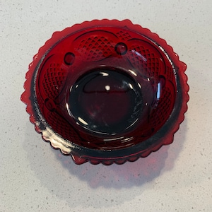 May include: A red glass bowl with a scalloped edge and a diamond pattern. The bowl is empty and has a reflective surface.