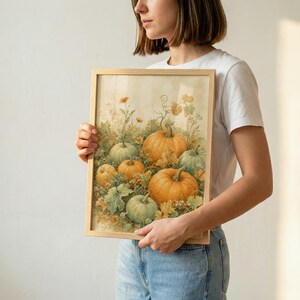 May include: A rectangular framed art print featuring a watercolor-style illustration of various pumpkins in shades of orange and muted green, surrounded by foliage and vines against a soft, light-colored background within a simple wooden frame.