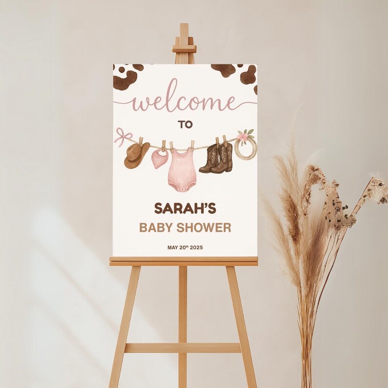 Może przedstawiać: Witamy na Baby Shower Sarah z brązowym tłem w krowie cętki. Na tablicy znajduje się sznurek do suszenia z r&oacute;żowym body dla dziecka, brązowym kowbojskim kapeluszem, r&oacute;żowym śliniakiem i dwiema parami brązowych kowbojskich but&oacute;w.