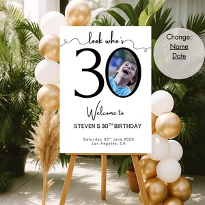 Peut inclure: Panneau blanc sur chevalet en bois avec le texte "look who's 30" et "Welcome to STEVEN S 30TH BIRTHDAY". Une photo d'une personne est dans le z&eacute;ro. Ballons dor&eacute;s et blancs et verdure en arri&egrave;re-plan.