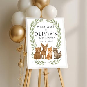 May include: Welcome to Olivia's Baby Shower sign with a green leafy wreath and woodland animals including a bear, moose, fox, and raccoon. The date is June 3rd, 202X.