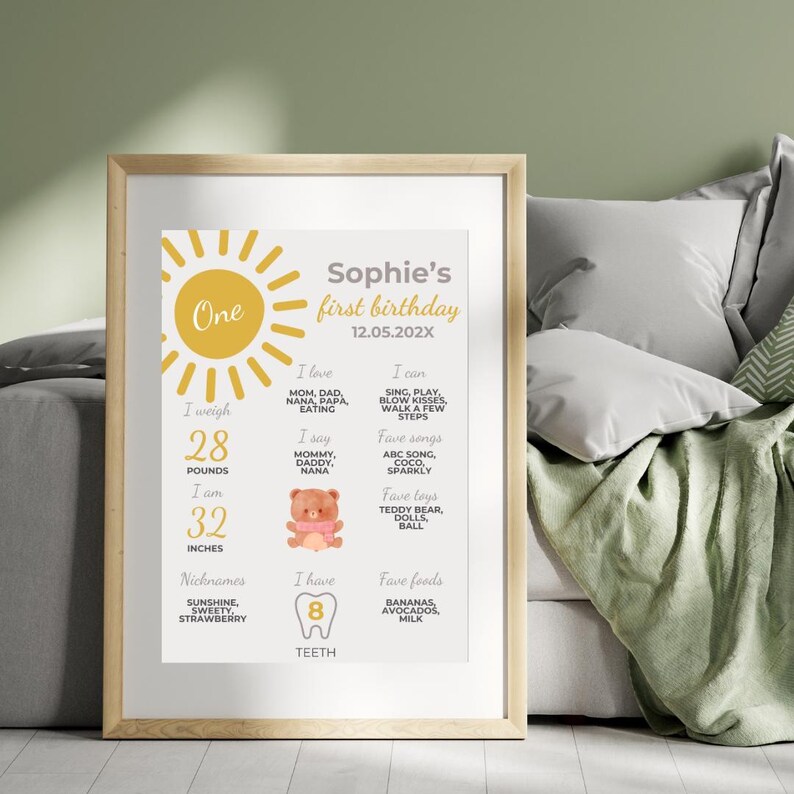 May include: A yellow sun with the word "One" inside, a white background with a gray border, and text that reads "Sophie's first birthday 12.05.202X". The text lists the child's weight (28 pounds), height (32 inches), favorite foods, songs, toys, and things they can do. The text also includes a list of nicknames, "Sunshine, Sweety, Strawberry", and the number of teeth, "8".