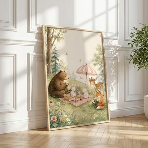 May include: A framed wall art print featuring a watercolor illustration of a brown bear, two white rabbits, a fawn, and a fox having a picnic on a grassy meadow. The scene includes a pink and white striped umbrella, wildflowers, and butterflies.