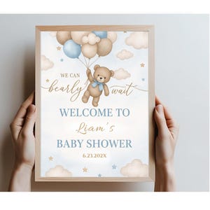 May include: A blue and brown baby shower welcome sign with a teddy bear holding balloons. The sign says "We can barely wait. Welcome to Liam's Baby Shower 6.23.202X".