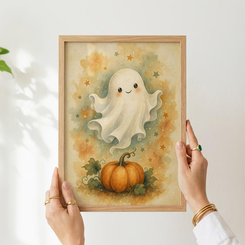 May include: A framed wall art print featuring a watercolor illustration of a smiling white ghost floating above an orange pumpkin with green leaves, set against a soft yellow and orange background decorated with small scattered stars.