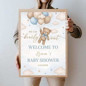 May include: A blue and brown baby shower welcome sign with a teddy bear holding balloons. The sign says "We can barely wait, Welcome to Liam's Baby Shower, 6.23.202X".