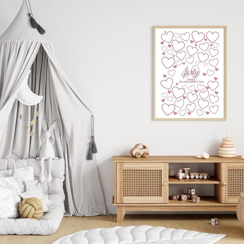 May include: A framed print with a light wood frame features a design of pink hearts on a white background. The text "forty things we love about you" is in the center. The print is displayed in a child's room with a wooden cabinet and toys.