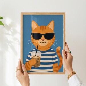 May include: A framed digital illustration of an orange tabby cat wearing black sunglasses and a blue and white striped shirt. The cat is holding a clear plastic cup filled with an iced coffee beverage against a solid blue background.