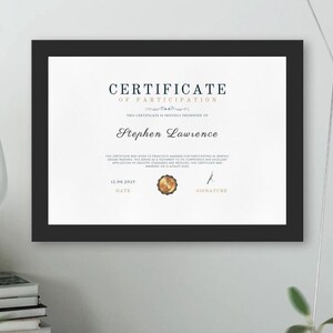 以下が含まれることがあります： 白い背景に「CERTIFICATE OF PARTICIPATION」と「Stephen Lawrence」の文字が印刷された、金色のシールと黒い額縁の参加証明書です。