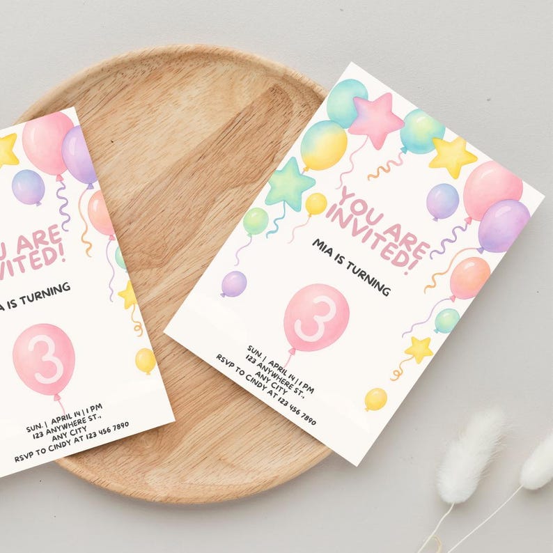 Op de afbeelding: Twee rechthoekige verjaardagsuitnodigingen met aquarelillustraties van pastelkleurige ballonnen en sterren. De tekst luidt YOU ARE INVITED! MIA IS TURNING 3, met details over het evenement, datum, tijd en RSVP-informatie eronder.
