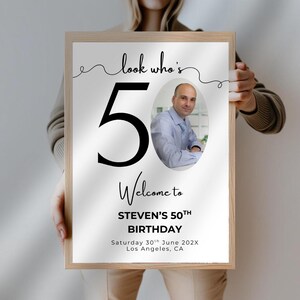 May include: A white poster with black text and a photo of a person. The text reads "look who's 50", "Welcome to STEVEN'S 50TH BIRTHDAY", "Saturday 30th June 202X", and "Los Angeles, CA".