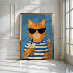 May include: A framed wall art print featuring an orange tabby cat wearing black sunglasses and a blue and white striped shirt. The cat is holding a clear plastic cup filled with an iced beverage and a black straw against a solid blue background.