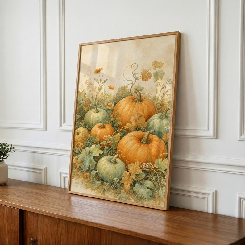 May include: A framed wall art print featuring a watercolor-style illustration of multiple orange and green pumpkins nestled among green leaves, vines, and small yellow flowers against a soft, neutral, cream-colored background.